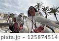 Mother and daughter feeding pigeons on a promenade 125874514