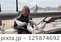 Blonde girl feeding pigeons on a promenade 125874692