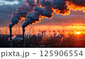 Industrial smokestacks release emissions against a vibrant sunset backdrop over a city skyline 125906554