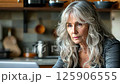 Focused older woman working on laptop in modern kitchen during day 125906555
