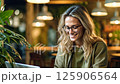 Smiling woman works on laptop at cozy cafe in afternoon light 125906564