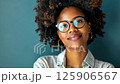 Confident young woman smiling against a blue background with natural curly hair 125906567