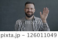 Slow motion portrait of friendly young man waving hand smiling looking at camera on black color background. People and expression concept. 126011049