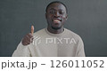 Slow motion portrait of happy African American man showing thumbs-up hand gesture smiling looking at camera on black color background 126011052