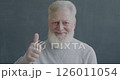 Slow motion portrait of pleased senior man showing thumbs-up hand gesture smiling looking at camera on black color background. 126011054
