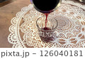 Wine is being poured in slow motion from a vessel into a clear glass resting on an intricately designed lace doily on a tavern table. 126040181