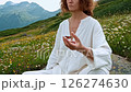 Woman white robe finds peace, deep meditation amidst vibrant mountain meadow. Serene meditation practice connects inner self nature's beauty. Such mindful meditation brings tranquility calm busy mind. 126274630