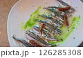 Overhead food panning from freshly made golden fries to marinated anchovies fish fillets artfully arranged on a white plate, garnished with vibrant green sauce and herbs. 126285308