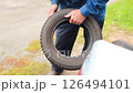Senior man takes out studless winter tires for a small car from the trunk of a car 126494101