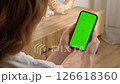 Woman use digital tech cell phone open green screen mock up. Hand press click phone web site middle center. Girl hold mobile. Turn on chroma key page. Cozy home background. Online app copy space. 126618360
