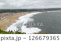 Dramatic coastal view showcases powerful waves crashing onto a sandy beach beside a quaint town under a moody sky. Evokes themes of natures force, travel, or remote locations. 126679365