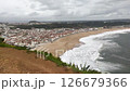 Scenic coastal townscape with a sandy beach and crashing waves under a cloudy sky. Evokes travel, vacation, nature, and seaside living concepts. Ideal for tourism ads. 126679366