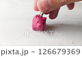 Saving money concept. Closeup shot of a hand placing a coin into a small, handcrafted pink piggy bank. Symbolizes savings, finance, investment, and economic growth. 126679369