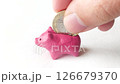 Concept shot showcasing a pink piggy bank, with a coin being dropped in. Illustrates savings, finance, economy, or childhood. Symbolizes financial planning and future security. 126679370