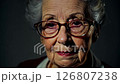 Close-up video of elderly woman with glasses, expressing confusion turning to wisdom, dramatic side lighting, static camera 126807238