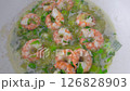 Juicy shrimps are simmering in a bubbling broth alongside green vegetables and herbs, creating a delightful culinary experience in a cheerful kitchen. 126828903