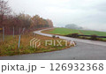 Rainy autumn landscape with asphalt winding road, bench and fog over green fields 126932368