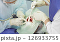 Two dental professionals perform a procedure on a patient in a clinical environment, focused and attentive to details 126933755