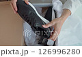 The fresh unboxing reveals new footwear: a pair of sleek black trainers is carefully extracted from their box, showing off their modern design and comfortable look. 126996280