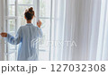 Morning lifestyle scene of a woman standing by the window opening the curtains. Healthy lifestyle. 127032308