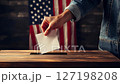 Person voting in USA presidential election, hand placing ballot in box with American flag in background. Patriotic concept, civic duty, democracy and political participation in a close-up election sce 127198208