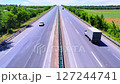 Straight highway through green fields with a few vehicles, including a truck, moving under clear sunny sky. Aerial view 127244741