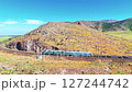Freight train with electric locomotive moves along winding railway through rocky hills in Southern Kazakhstan under clear summer sky 127244742