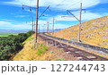 Railway bends around a hillside, stretching into the distance among green fields and mountains under a bright sunny sky 127244743