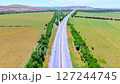 A straight highway through green fields and hills, captured from above. Summer day, clear weather, cars on the road 127244745