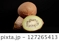 Close-Up of Fresh Kiwi Fruits with Fuzzy Brown Skin and Vibrant Green Slices on Black Background 127265413