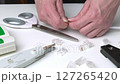 Close-up of hands cutting Ethernet cable wires on white desk with networking tools scattered around 127265420