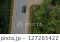 Aerial View of Black Car Driving Past Lush Greenery on Quiet Country Road in Daylight 127265422