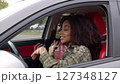 Positive carefree beautiful African American female driver with Afro hairstyle sitting in vehicle, enjoying catching music, singing along and swaying to the beat while driving car in city street. 127348127
