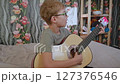 A teenage boy plays the guitar on the sofa. Active children's recreation. Let's learn to play the guitar 127376546