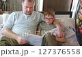 Father hugs his little school-age son and reads funny paper literature. Happy little boy reading a book, enjoying his free weekend with his joyful father on the sofa. 127376558