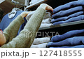 Woman choosing grey sweater on clothes shelf in fashion store 127418555