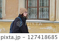 Confident redhead student walking near university building during cold winter day, wearing glasses, beanie, black winter coat and carrying backpack while moving along campus exterior 127418685