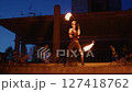 Fire dancer performing captivating skills with flaming torches, illuminating decaying architectural backdrop during twilight's dramatic transition between day and night 127418762
