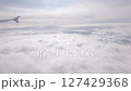Clouds in sky. Plane flight over white cloud and sunbeams at high up sky. Fly in clear soft clouds at sunny light day, looking from airplane window 127429368
