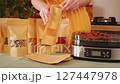 Woman packs dried fruit and mushrooms into kraft paper bags, next to a modern food dehydrator 127447978