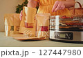 Woman carefully placing dried fruits and vegetables into paper bags, next to a food dehydrator 127447980