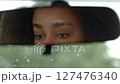 Reflection of attractive black female driver in car rear view mirror, looking with radiant smile, expressing cheerful mood and friendliness while travelling by vehicle during road trip.. 127476340