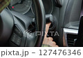 Close up of female finger pressing car engine start button, firmly holding steering wheel and beginning road trip . Rear view. 127476346
