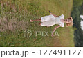 Young girl in white dress running along country road in summer field 127491127