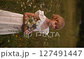 Young blonde girl in white dress standing in a field, holding a bouquet of flowers 127491447