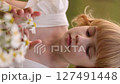 Young blonde girl in white dress picking a bouquet of daisies in a summer field. 127491448