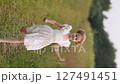 Young girl in white dress running along country road in summer field 127491451