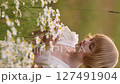 Young blonde girl in white dress picking a bouquet of daisies in a summer field. 127491904
