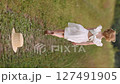 Young girl in white dress running along country road in summer field 127491905