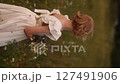 Young blonde girl in white dress standing in a field, holding a bouquet of flowers 127491906